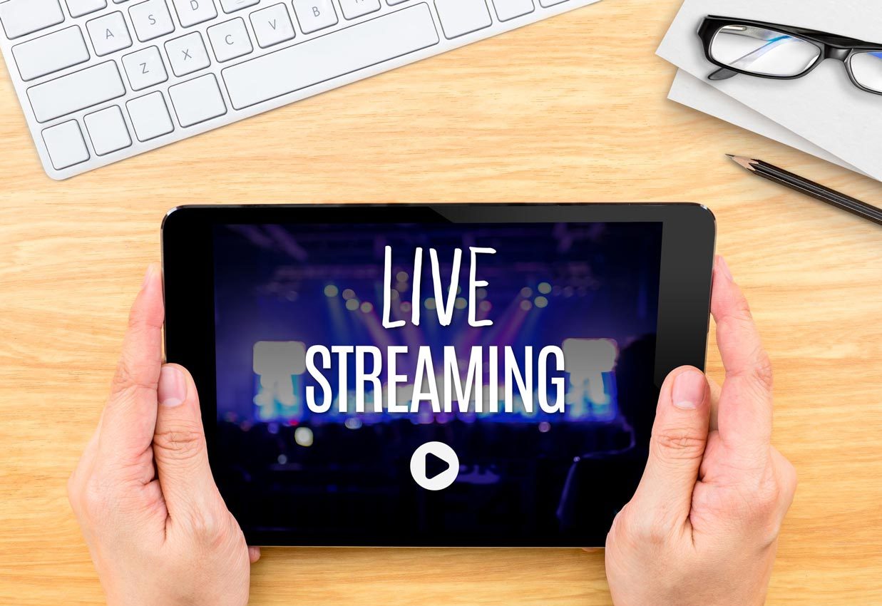 Hände die ein Tablet auf dem Schreibtisch festhalten und Live Streaming schauen.