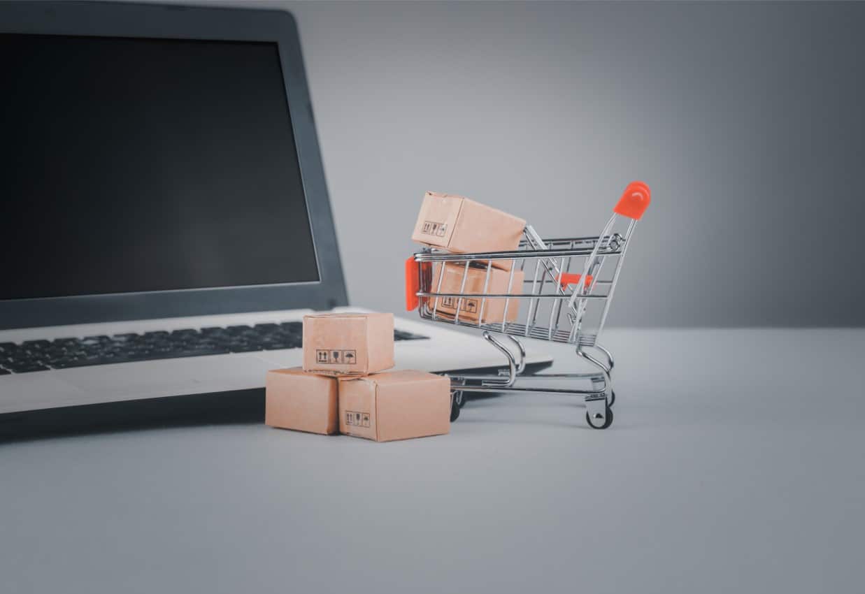 Online Shop Tipps , Kleiner Einkaufswagen mit Kartons vor einem Laptop stehend